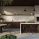 Modern outdoor kitchen with bar stools, dining table, fireplace, and lush surrounding greenery.